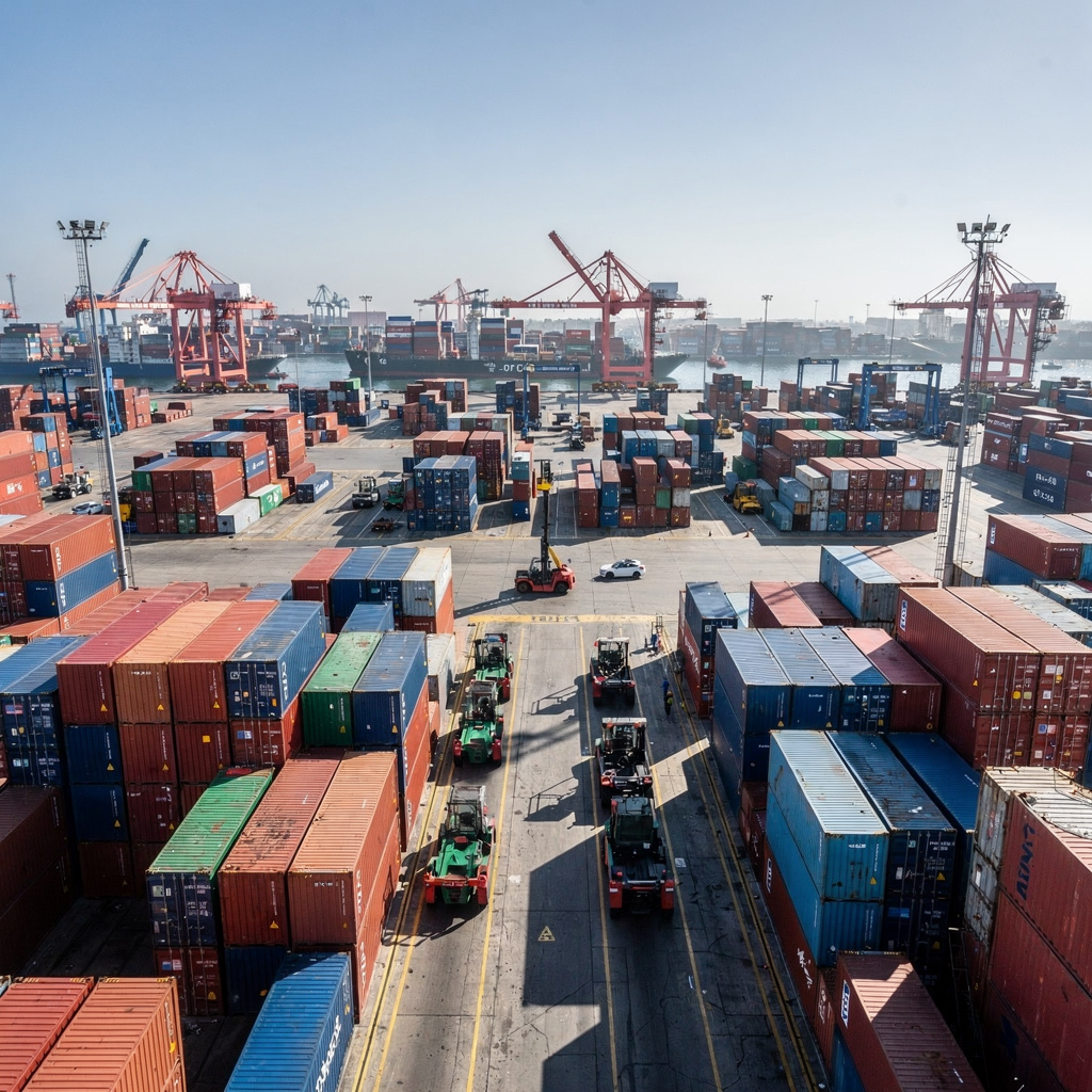 Aerial view of container storage and RTG cranes Aerial view of a busy port storage area with stacked containers, RTG cranes working, and automated guided vehicles moving between rows, clear bright day, no text or numbers