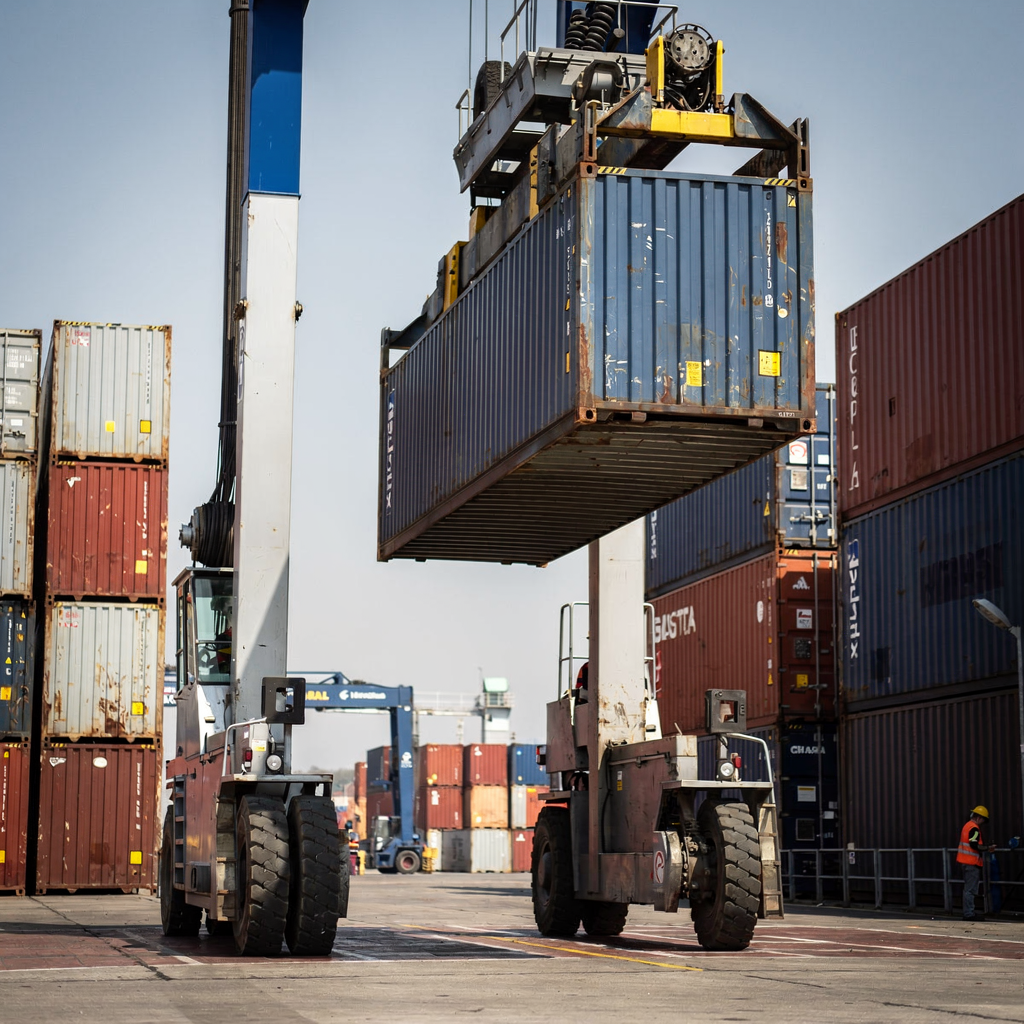 Automated stacking crane lifting a container Close-up of an automated stacking crane in a container yard lifting a container, with operators in the distance and clear sky, no text