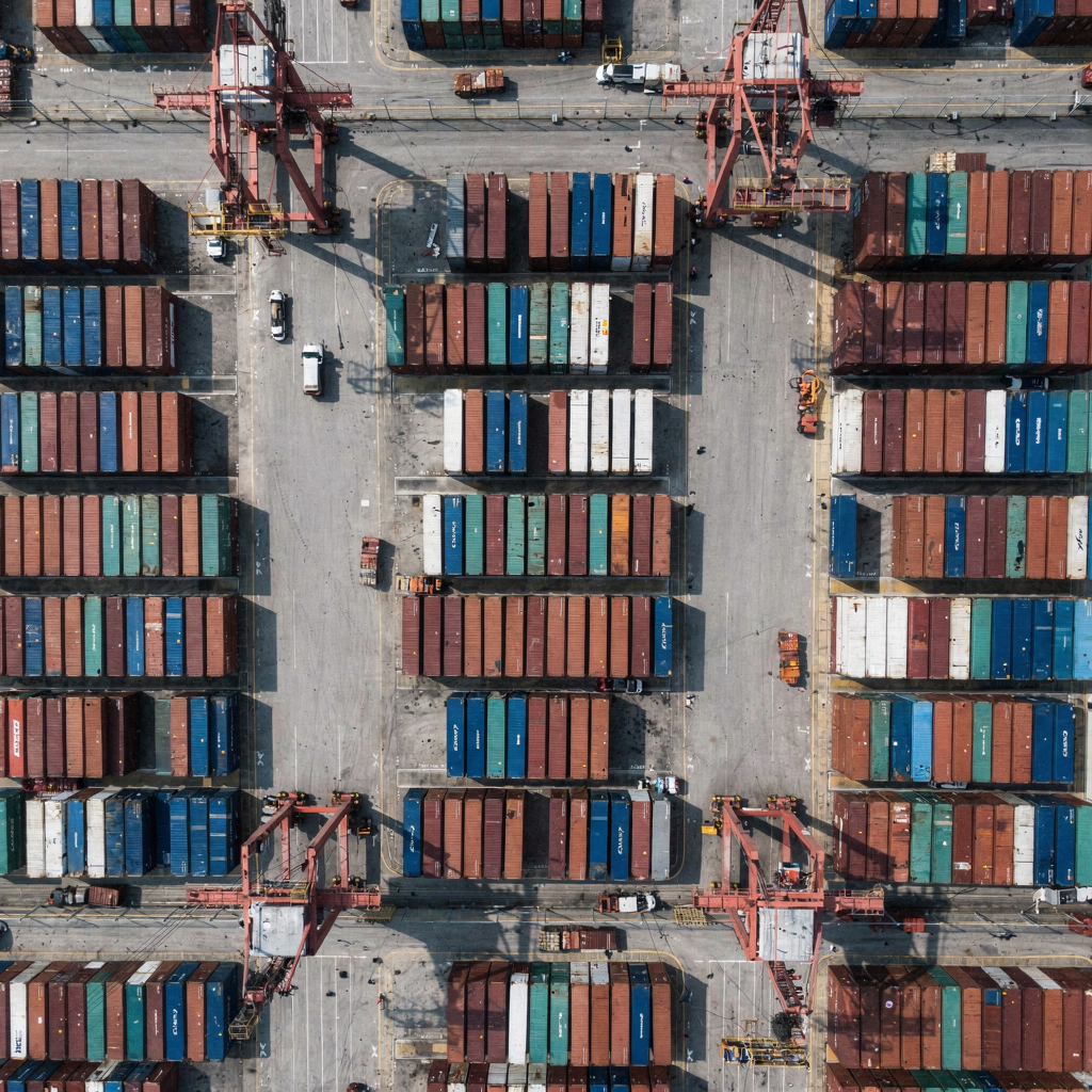 Container yard with cranes and color-grouped stacks A top-down view of a container yard with cranes and stacked containers, showing clear lanes and different container groups by color, daytime, tidy layout
