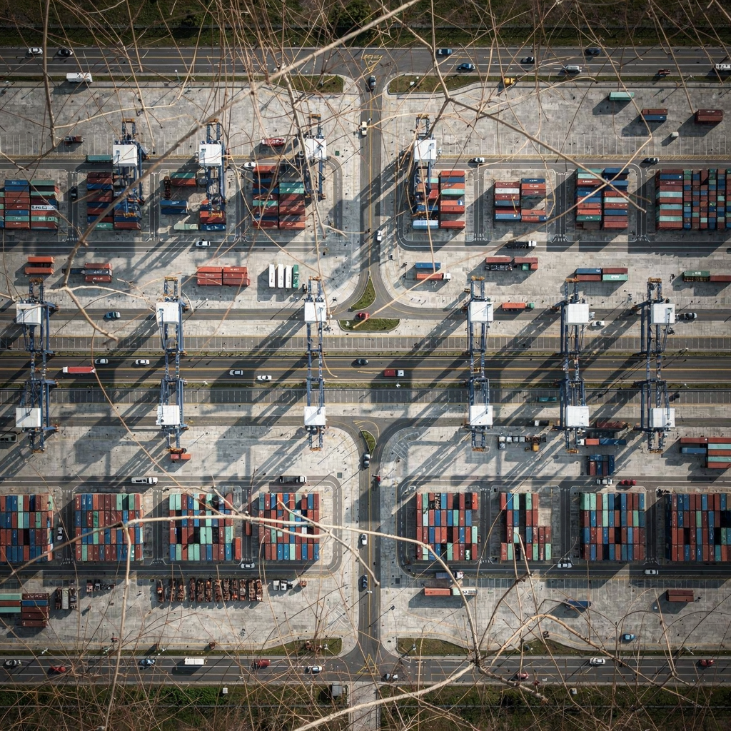 Terminal map with AGV routes A modern container terminal map showing lanes, quay cranes, yard blocks, and AGV moving along defined paths; overhead view with clear roads, cranes, storage blocks, and no text